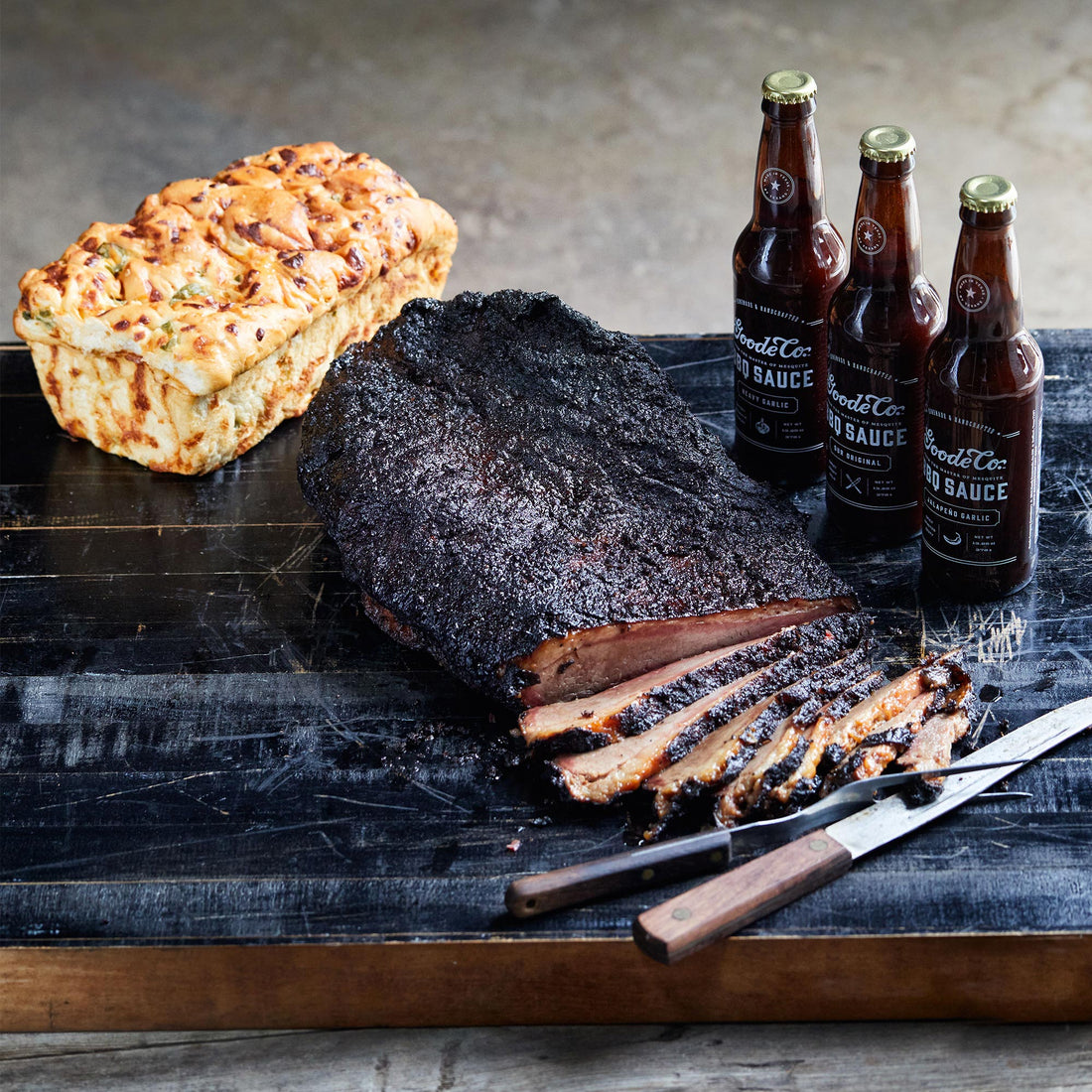 sliced brisket on a black cutting board with a knife resting on the side and a sliced loaf of bread on the other.
