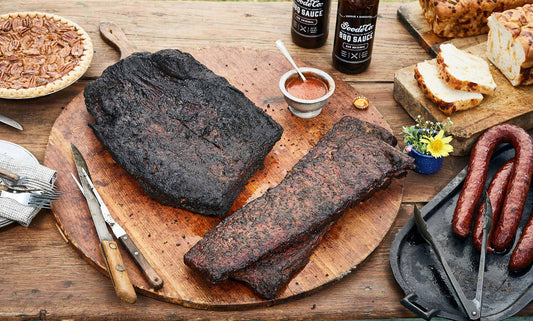 Brisket and ribs on a wooden cutting board with sausage to the side and a pecan pie in the background.