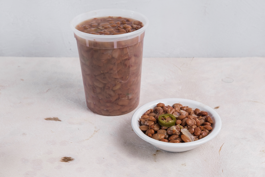 A close-up of a bowl of beans and a quart of baked beans in the background