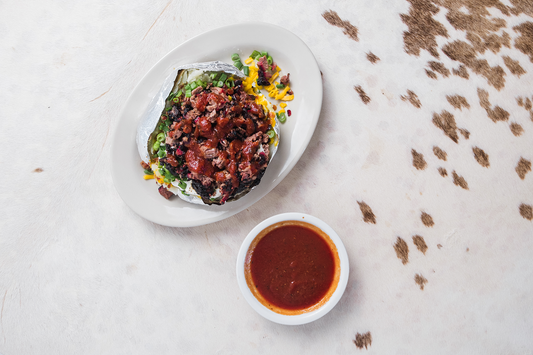 Stuffed baked potato with sliced brisket, shredded cheese, and green onions on it.