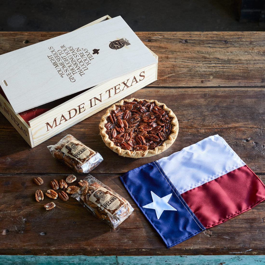 A full pecan pie, Texas state flag, a bag of sliced pecans open on the table, and a “Made in Texas” pecan pie box open.