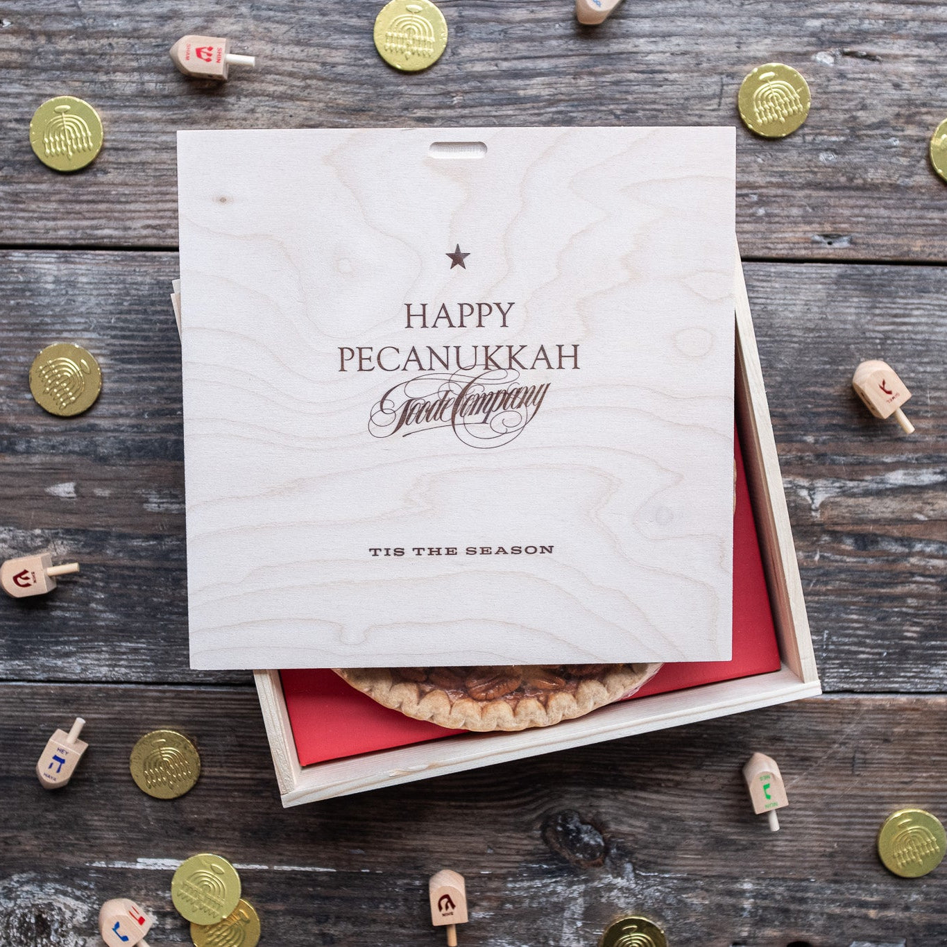 Pecanukkah gift box with pecan pie on a wooden surface with Hanukkah menorahs and gelt.